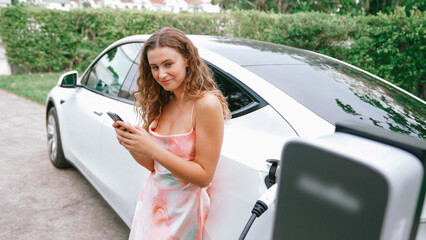 Young woman use smartphone to pay for electricity at public EV car charging station in nature....