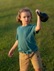 Child lifting the kettlebell in backyard outside. Child boy working out with dumbbells. Kids sport and active healthy life. Sport and kids training.