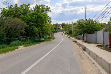 A road with a fence on the side and a house in the distance