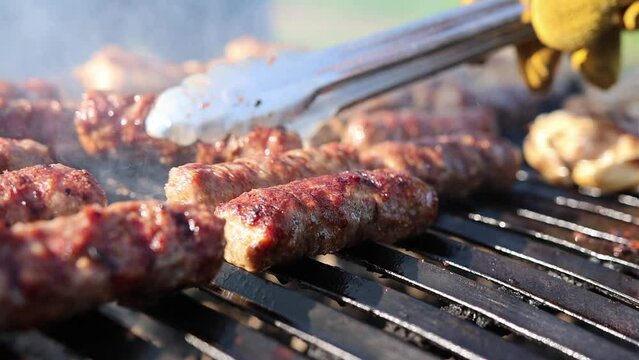 Person With A Tong Grilling Balkan Sausage Outdoor. Close-up Shot