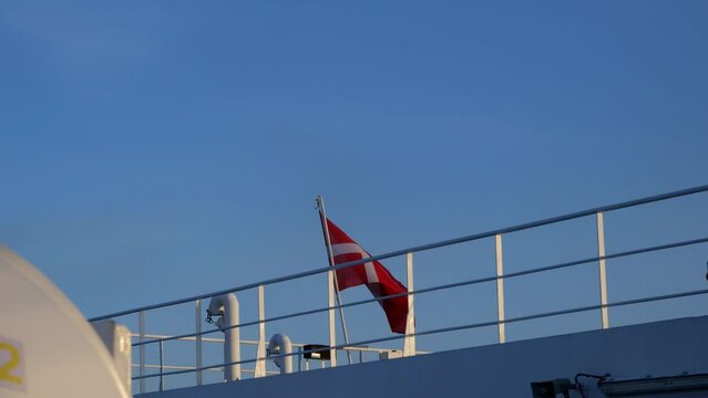 Danish national flag fluttering hung on a metal mast on the upper deck of a ferry, beautiful sunny evening