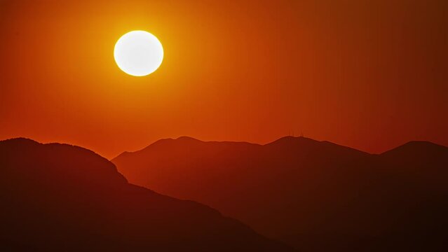 Glowing golden sun setting behind the silhouette of a mountainous landscape - time lapse