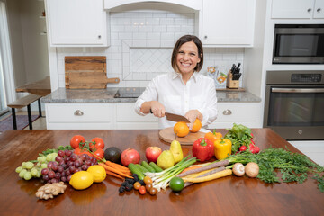 Friendly looking woman with brown bob chopping fruit in kitchen