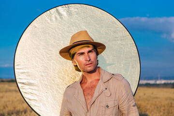 Portrait of a tall handsome man dressed in a coarse linen suit and hat standing at golden oat field...