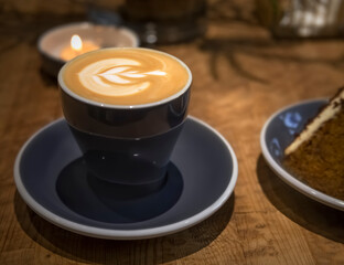 A cup of art cappuccino and a candle on a wooden table in the cafeteria