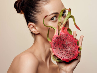 Young woman holding colorful dragon fruit in front of face with open mouth in playful expression