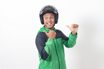 Portrait of Asian online taxi driver wearing green jacket and helmet pointing at empty space with finger. Isolated image on white background