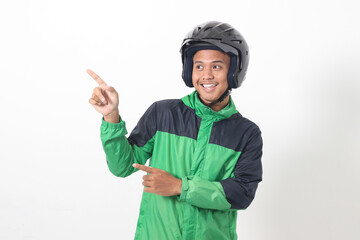 Portrait of Asian online taxi driver wearing green jacket and helmet pointing at empty space with finger. Isolated image on white background