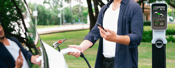 Man using smartphone online banking application to pay for electric car battery charging from EV...