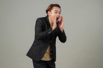 portrait of happy asian businessman wearing suit shouting with cupping hand on isolated background