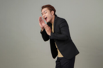 portrait of happy asian businessman wearing suit shouting with cupping hand on isolated background