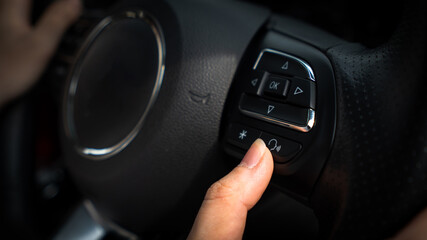 Finger of driver pushing on speaker phone button on steering wheel of car. Technology and safety transportation concept. 