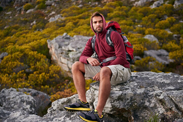 Man, mountain and hiking in nature for rest and fitness for wellness and exercise for training and adventure in environment. Young person, sitting with backpack on rock for workout and trekking
