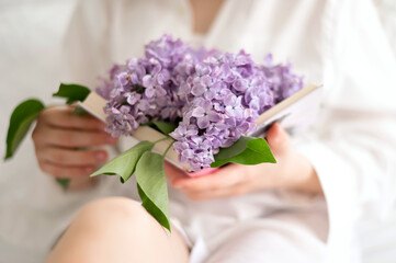 Open book with lilac flowers between pages in girl hands, soft natural light, aesthetic floral...