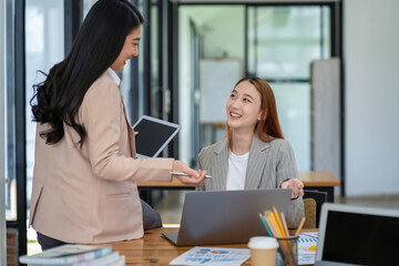 Two Asian businesswomen working Creative discussion in office using laptop and tablet, business concept