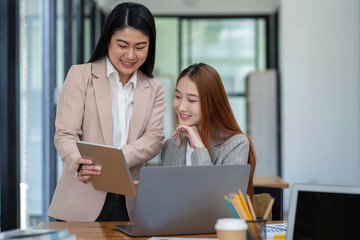 Two Asian businesswomen working Creative discussion in office using laptop and tablet, business concept