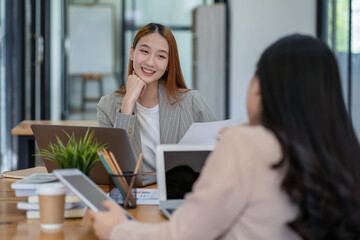 Two Asian businesswomen working Creative discussion in office using laptop and tablet, business concept