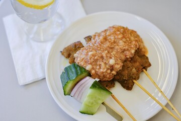 A plate of traditional Malaysian chicken sate skewers with peanut sauce, rice cakes, sliced...
