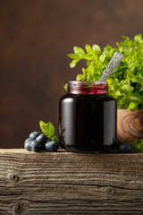 Jar of blueberry jam with fresh berries on an old wooden table.