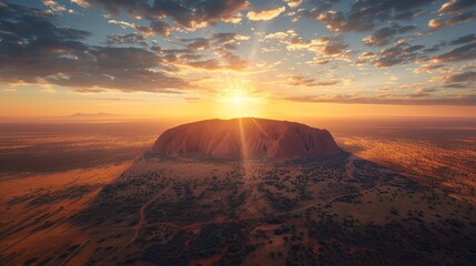 Aerial view of Uluru (Ayers Rock) in Australia, with its massive red sandstone formation rising from the flat desert landscape at sunset.      - Powered by Adobe