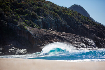 Crystal blue turquoise wave breaking along a sandy shoreline below sloping mountains on the East...
