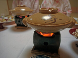 Cooking japanese nabe soup on fire in ceramic hot pot on traditional shichirin stove for fancy traditional ryokan dinner for two, couple in yukata in defocused background