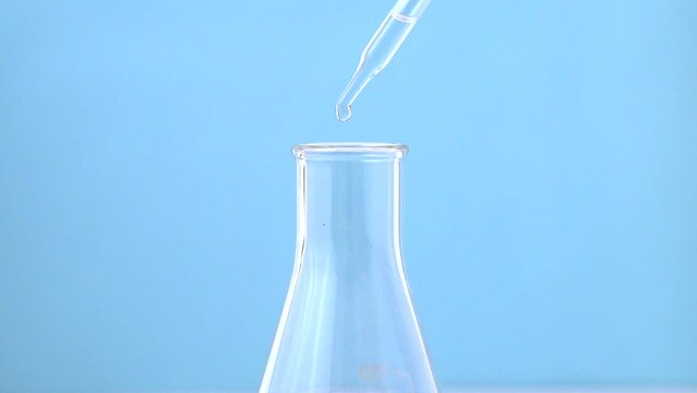 Macro video of dropper & beaker on plain background. Close up of scientific lab equipments on coloured background.