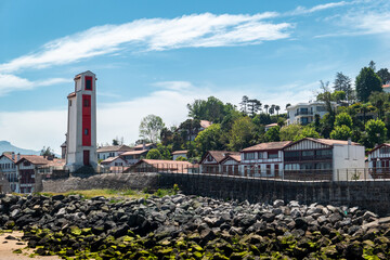 Em meio a um céu azul e parte de cidade de Saint Jean de Luz, um farol à beira mar para orientação da navegação marítima © LuIvDa