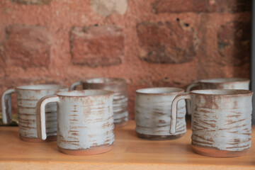 Tableware mugs displayed on hardwood shelf against brick wall