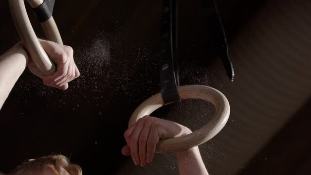 Closeup slomo of blond male athlete doing pull up in gym with gymnastic rings