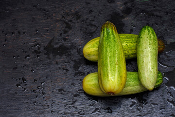 Few fresh organic cucumbers on a black background with selective focus.