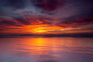 Crimson sunrise reflecting over shallow ocean shoreline