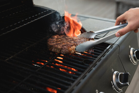 Person flipping medium steak with grill marks & flames on grill