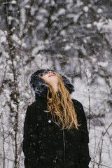 Blond girl with tongue out catching snow flakes falling in forest