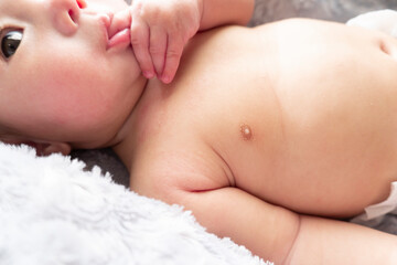 Naked Japanese baby boy with red dry skin lies down on a comfortable gray bed and sucks his thumb