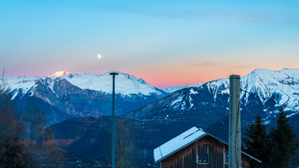 Lever de soleil sur les montagnes enneigées des alpes à la Toussuire avec un chalet au premier plan et des couleurs rougeoyantes dans le ciel