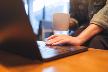 Closeup image of a woman working and touching on laptop computer touchpad while drinking coffee in cafe