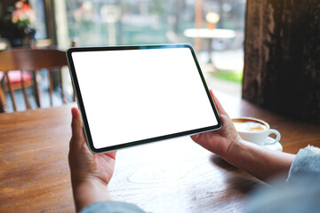 Mockup image of a woman holding digital tablet with blank white desktop screen in cafe