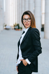 Confident businesswoman in a sharp suit standing in an urban environment, projecting...