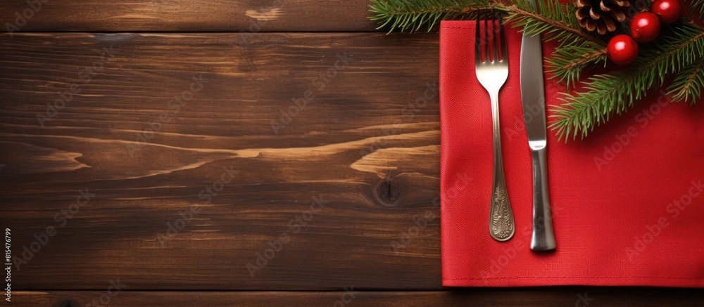 Poster Top view of a red napkin with a wooden background showcasing a spoon knife and fork alongside a fir tree branch Ample copy space available for showcasing your content such as a menu or advertising