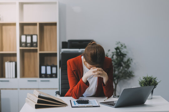 Asian women sitting in a home office With stress and eye strain.Tired businesswoman holding eyeglasses and massaging nose bridge. There are tablets, laptops, and coffee.
