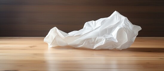 A crumpled white sheet of paper is seen in a lumpy state on a wooden floor creating a copy space image