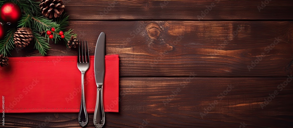 Poster Top view of a red napkin with a wooden background showcasing a spoon knife and fork alongside a fir tree branch Ample copy space available for showcasing your content such as a menu or advertising