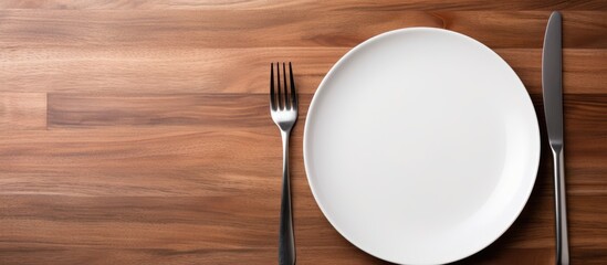 A concept image of white plate fork and knife placed on a wooden table along with cutlery and silverware. Creative banner. Copyspace image