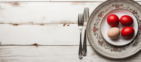 A top down view of a plate with vintage silverware and red Easter eggs on a white shabby wooden table creating a visually appealing copy space image