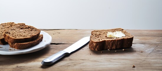 On a white wooden table there is a copy space image featuring a slice of brown bread accompanied by a butter spread with an old knife nearby