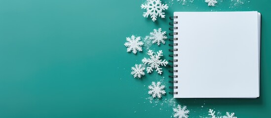 The image depicts an open notebook alongside delicate snowflakes set against a vibrant green background This top down view offers ample space for personalization or additional elements