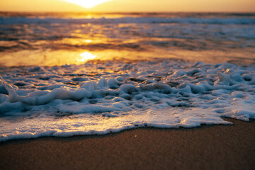 Foamy waves wash along the shore on sunrise