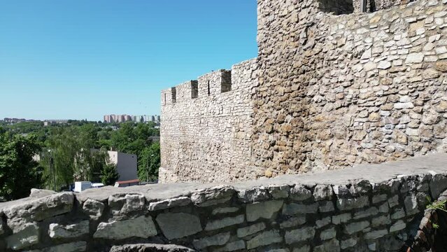 Medieval Bedzin castle with a turret, white stone walls, and courtyard during a beautiful summer day surrounded by lush greenery, under a clear blue sky.