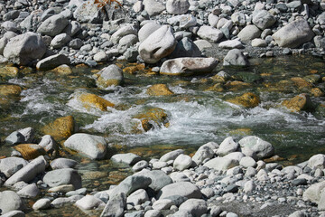 shallow stream flows over rocky bed, creating tranquil and natural scene. clear water, reflecting sunlight, moves around rocks, motion. brightness and blurred effect contribute to serene atmosphere - Powered by Adobe